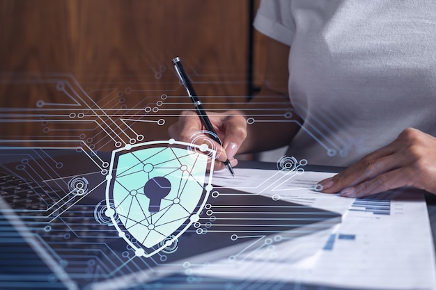 Eine Geschäftsfrau in Freizeitkleidung, die den Vertrag unterzeichnet, um die Wahrscheinlichkeit von Risiken bei der Cybersicherheit zu verhindern Vorhängeschloss-Hologramm-Symbole über dem Arbeitstisch