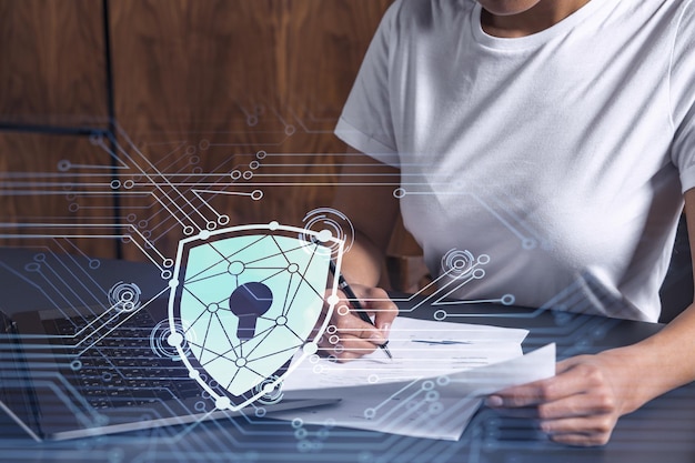Eine Geschäftsfrau in Freizeitkleidung, die den Vertrag unterzeichnet, um die Wahrscheinlichkeit von Risiken bei der Cybersicherheit zu verhindern Vorhängeschloss-Hologramm-Symbole über dem Arbeitstisch