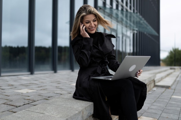 Eine Geschäftsfrau mittleren Alters arbeitet online an einem Laptop vor dem Hintergrund eines Bürogebäudes