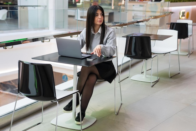 Eine Geschäftsfrau sitzt auf einem Tisch in einem Café Eine junge freiberufliche Frau arbeitet in einem Einkaufszentrum