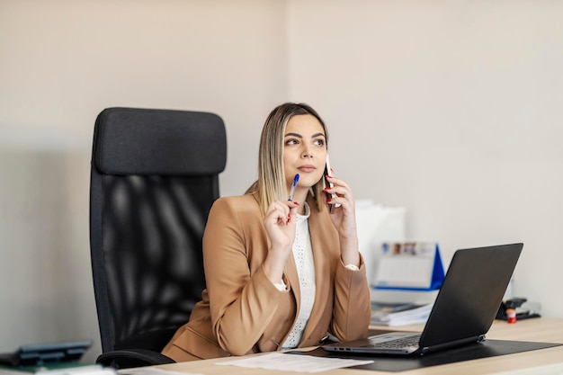 Eine Geschäftsfrau sitzt in Gesellschaft im Büro und führt ein Telefongespräch mit einem Partner