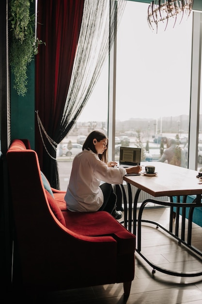 Foto eine geschäftsfrau sitzt mit dokumenten an einem tisch in einem café und arbeitet an einem laptop