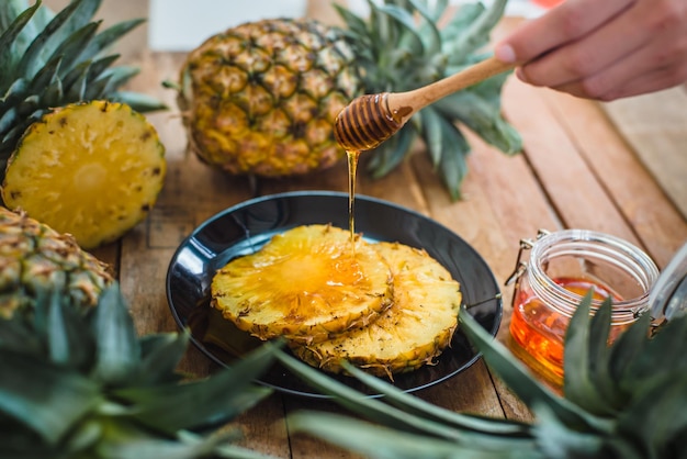 Foto eine geschnittene hand, die honig auf eine ananas-scheibe gießt