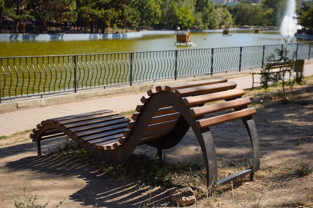 Eine geschwungene geschwungene dekorative Holzbank aus Brettern steht in einem Sommerpark leer