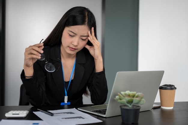 Eine gestresste asiatische Geschäftsfrau machte sich Sorgen über die Deadline ihres Projekts, während sie an ihrem Schreibtisch saß