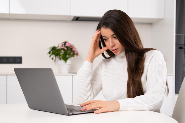 Eine gestresste junge Frau denkt intensiv nach, während sie zu Hause am Computer arbeitet