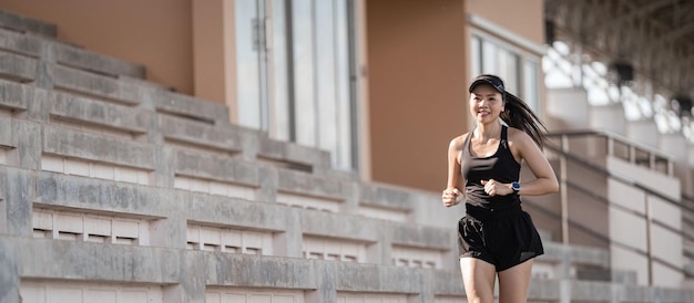 Eine gesunde erwachsene asiatische Frau, die auf die Betontreppe des Stadtstadions rennt, um den Körper zu stärken