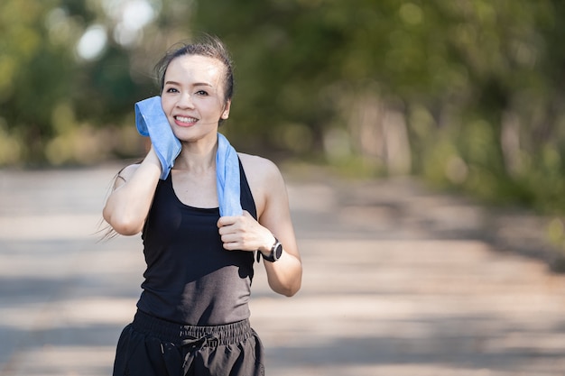 Eine gesunde glückliche asiatische Läuferin in schwarzen Sportoutfits, die im natürlichen Stadtpark unter abendlichem Sonnenuntergang joggt