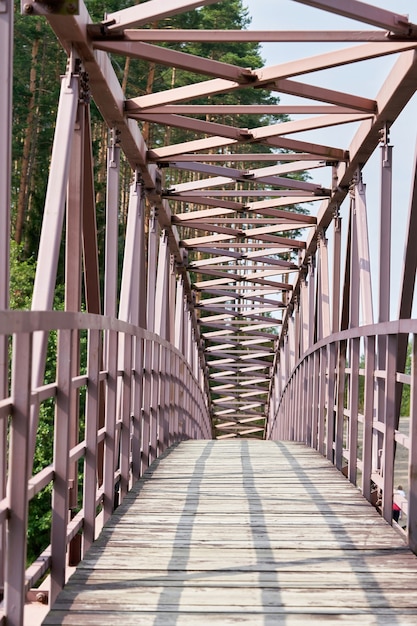 Eine gewölbte Fußgängerbrücke über den Fluss mit einem Holzdeck. Holzbrücke mit Eisengeländer