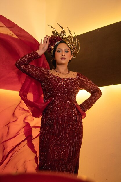 Eine Glamour-Frau posiert mit einem fliegenden roten Kleid auf ihrem Körper, während sie eine goldene Krone trägt