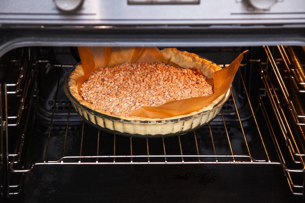 Eine Glasauflaufform mit Mürbeteig mit getrockneten Erbsen wird im Ofen gebacken