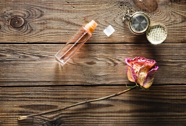 Eine Glasflasche mit Parfüm, trockener Rose, Vintage Taschenuhr auf einem rustikalen Holztisch. Draufsicht.