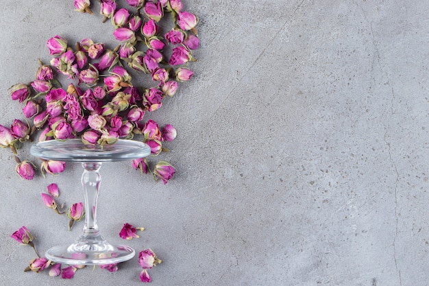 Eine Glasplatte voller getrockneter Rosenblütenknospen auf Steinhintergrund.