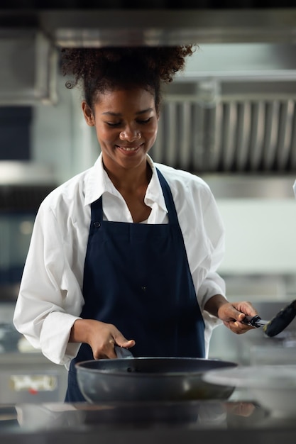 Eine glückliche afroamerikanische Frau steht mit gekreuzten Armen, während sie als Koch in einem Restaurant arbeitet.