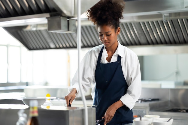 Eine glückliche afroamerikanische Frau steht mit gekreuzten Armen, während sie als Koch in einem Restaurant arbeitet.