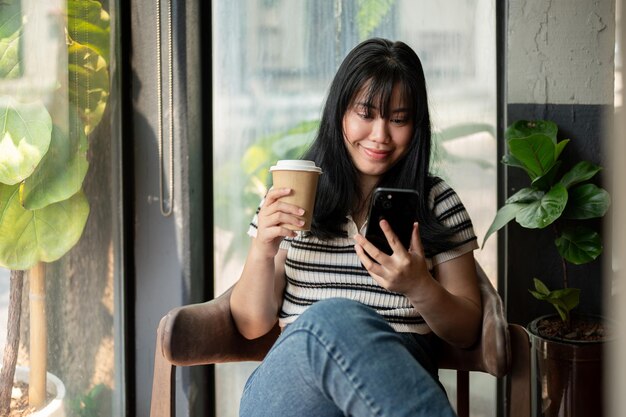 Foto eine glückliche asiatische frau entspannt sich in einem café mit ihrem smartphone und genießt ihren kaffee