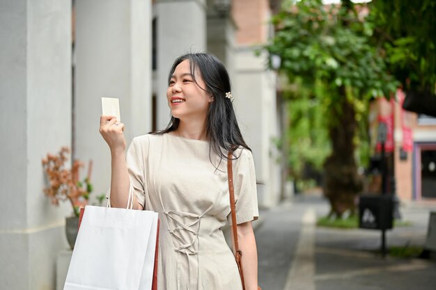 Eine glückliche asiatische Frau genießt ihren Einkaufstag in der Stadt und hält ihre Kreditkarte in der Hand
