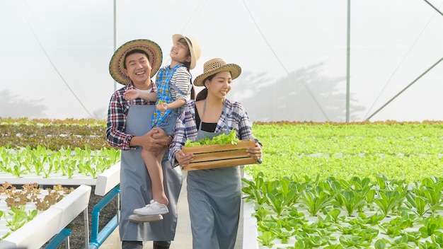 Eine glückliche Bauernfamilie, die in einer hydroponischen Gewächshausfarm arbeitet, sauberes Essen und gesundes Ernährungskonzept