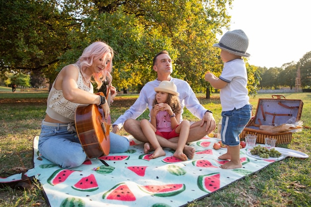 Eine glückliche Familie auf einem Picknick Mutter spielt Gitarre und Vater spielt mit den Kindern