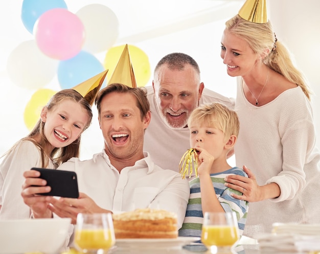Eine glückliche Familie, die einen Geburtstag mit einer Party feiert, die Hüte trägt und ein Selfie mit einem Telefon macht Reifer Mann, der auf einer Party ein Foto von seiner Vaterfrau und seinen Kindern macht, während er besondere Erinnerungen macht