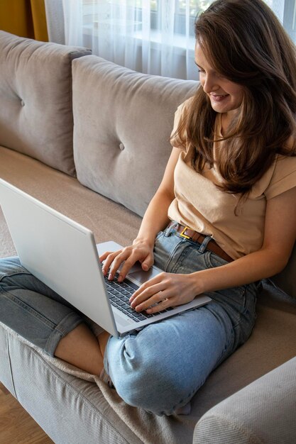 Eine glückliche Frau arbeitet remote mit einem Laptop auf einem Sofa Bequemer Arbeitsplatz in einer gemütlichen und stilvollen Wohnung