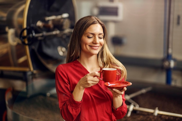 Eine glückliche Frau, die eine Tasse Kaffee in der Kaffeefabrik genießt