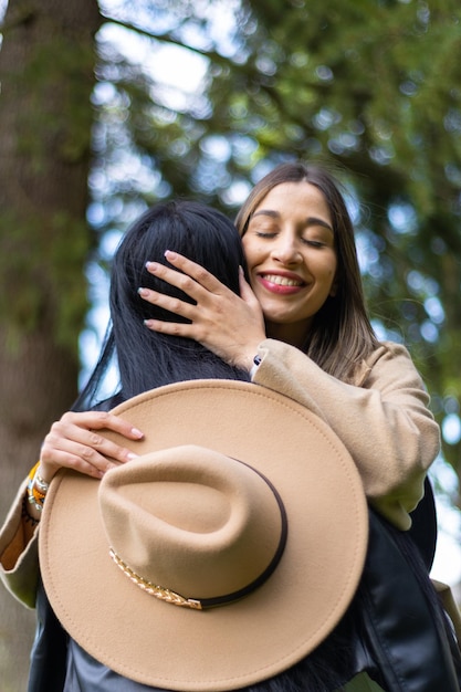 Eine glückliche Frau, die ihre Freundin im Park umarmt, während sie ihren Hut hält