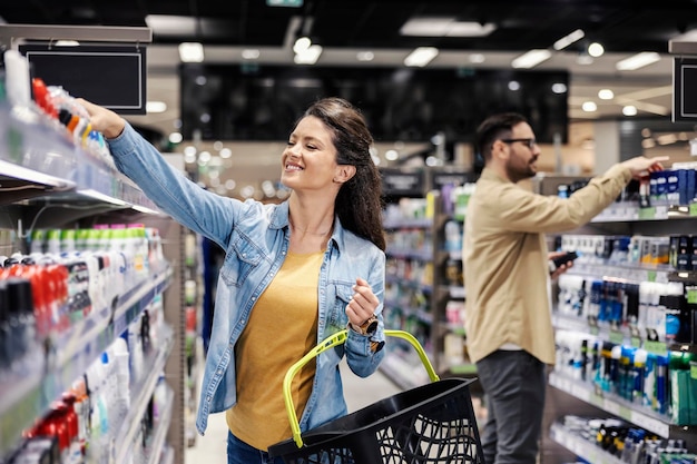 Eine glückliche Frau, die sich im Supermarkt für Deodorant entscheidet