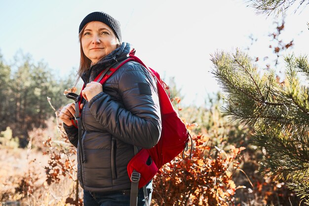 Foto eine glückliche frau genießt eine wanderung an einem sonnigen urlaubstag. eine frau mit rucksack geht durch den wald.