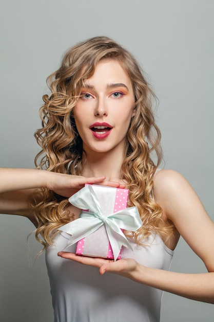 Eine glückliche Frau hält ein rosa Geschenk mit einem weißen seidenartigen Band