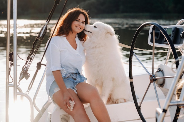 Eine glückliche Frau mit einem großen weißen Hund auf einer weißen Yacht auf See. Der Hund flüstert mir ins Ohr