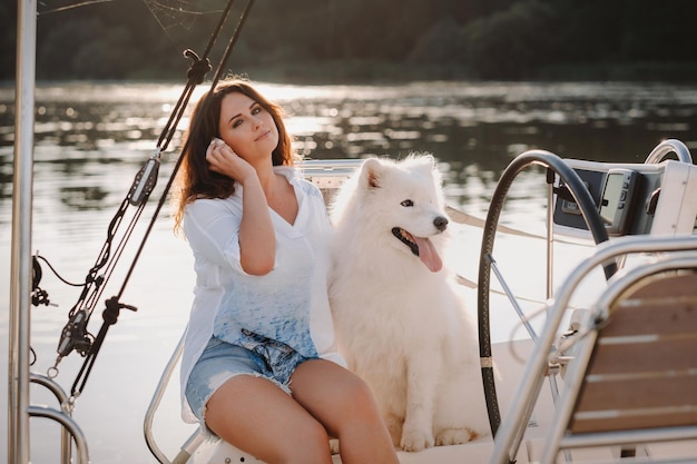 Eine glückliche Frau mit einem großen weißen Hund auf einer weißen Yacht im Meer.