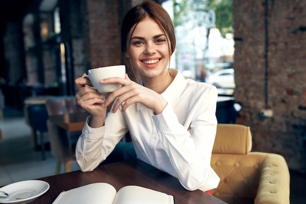 Eine glückliche Frau mit einer Tasse in der Hand sitzt auf einem Stuhl im Restaurant und das Innere im Hintergrund ist ein Foto in hoher Qualität