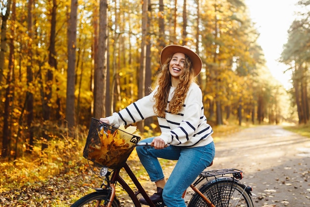 Eine glückliche Frau mit lockigem Haar fährt im sonnigen Herbstpark mit dem Fahrrad.