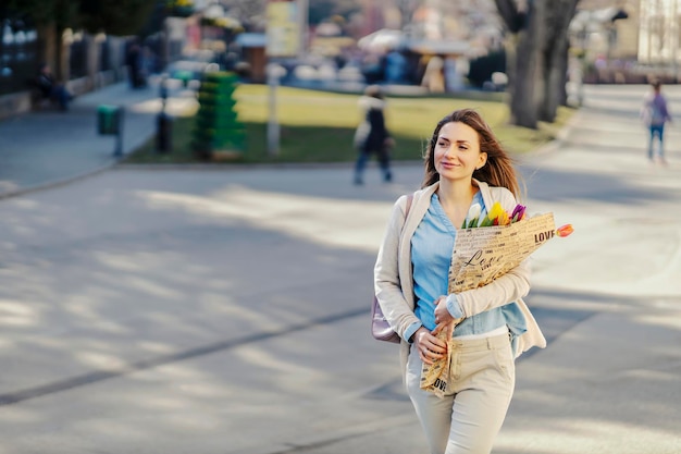 Eine glückliche Frau trägt Blumen in einem Park, den sie als Geschenk bekam