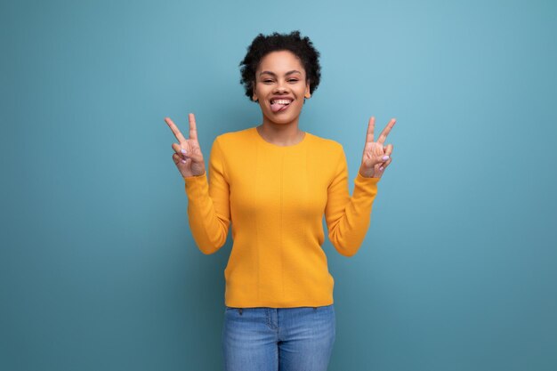 Eine glückliche, hübsche junge hispanische Frau mit schwarzem, lockigem Haar in einem gelben Pullover auf einem blauen Hintergrund