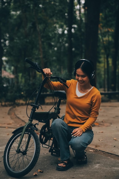 Eine glückliche junge asiatische Frau fährt in einem Stadtpark mit einem Fahrrad und lächelt, während sie das umweltfreundliche Verkehrskonzept Fahrrad benutzt.