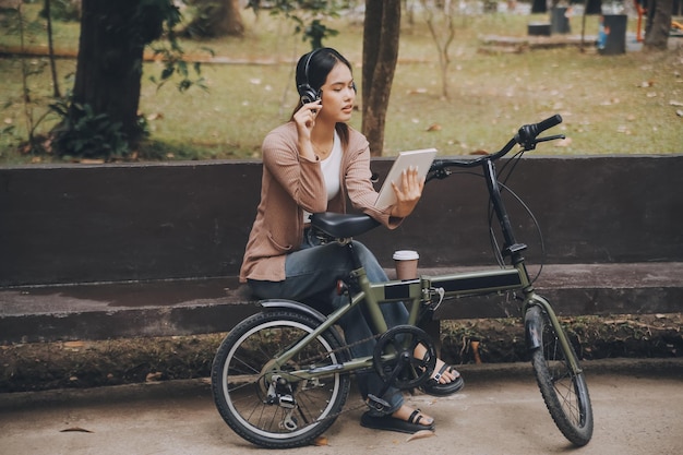 Eine glückliche junge asiatische Frau fährt in einem Stadtpark mit einem Fahrrad und lächelt, während sie das umweltfreundliche Verkehrskonzept Fahrrad benutzt.