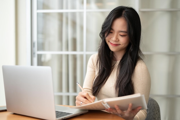 Eine glückliche junge asiatische Studentin konzentriert sich darauf, zu Hause online zu studieren