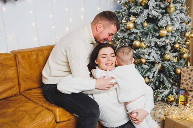 Eine glückliche junge Familie mit einem kleinen Kind feiert das neue Jahr zu Hause in der Nähe des Weihnachtsbaums. Weihnachten mit der Familie. Zeit zum Feiern des neuen Jahres