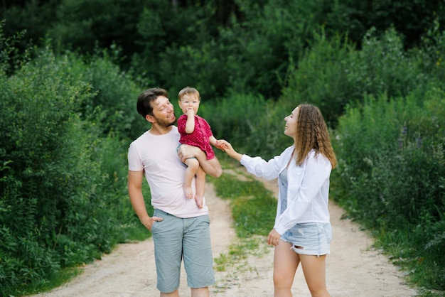 Eine glückliche junge Familie mit ihrem Sohn im Arm geht einen Waldweg entlang und genießt