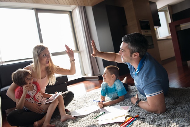 Eine glückliche junge Familie spielt zu Hause zusammen auf dem Boden mit einem Tablet und einem Zeichensatz für Kinder