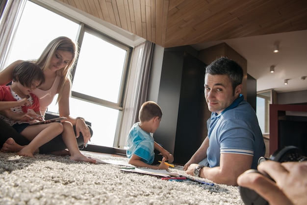 Eine glückliche junge Familie spielt zu Hause zusammen auf dem Boden mit einem Tablet und einem Zeichensatz für Kinder