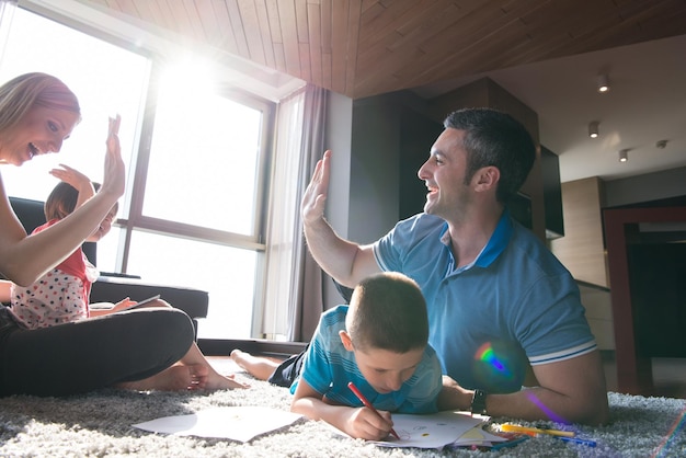 Eine glückliche junge Familie spielt zu Hause zusammen auf dem Boden mit einem Tablet und einem Zeichensatz für Kinder