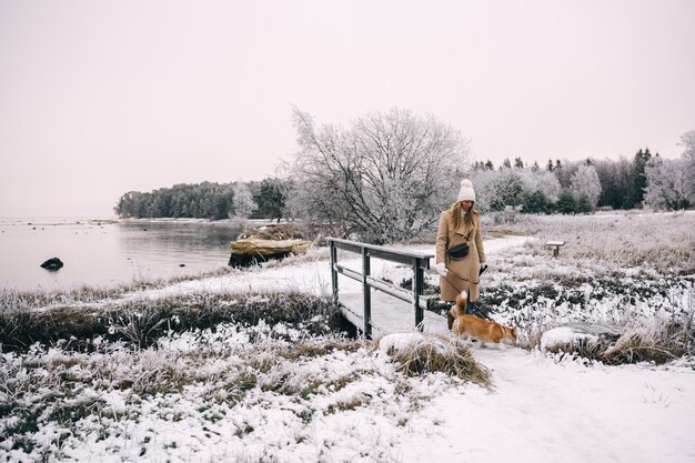 Eine glückliche junge Frau geht mit ihrem Welsh Corgi Pembroke Welpen durch die Natur im Winter