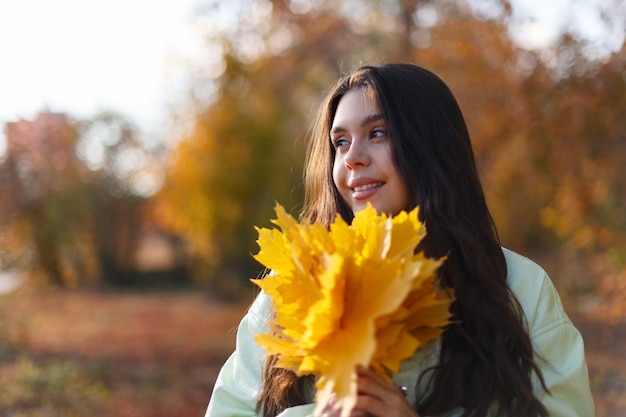 Eine glückliche junge Frau in einem Herbstpark mit einem Haufen Ahornblätter in den Händen