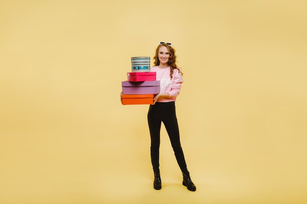 Eine glückliche junge Frau mit bunten Papierboxen nach dem Einkaufen lokalisiert auf einer Orange