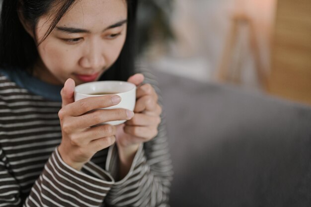 Eine glückliche junge Frau sitzt auf der Couch und genießt ihren morgendlichen Kaffee im Wohnzimmer