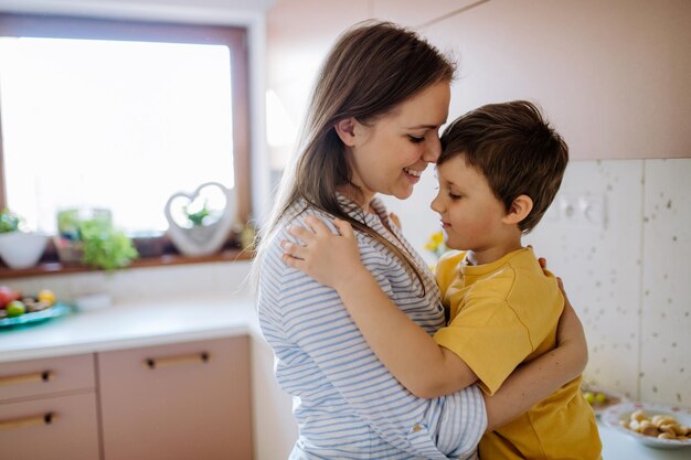 Eine glückliche junge Mutter umarmt ihren kleinen Sohn in der Küche zu Hause