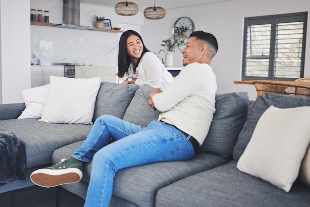 Eine glückliche Liebe und ein Paar entspannen sich auf dem Sofa und unterhalten sich und genießen das gemeinsame Wochenende in ihrem Zuhause. Lächelnde Unterhaltung und Frau mit Mann im Wohnzimmer lachen und haben Spaß beim Reden und Entspannen